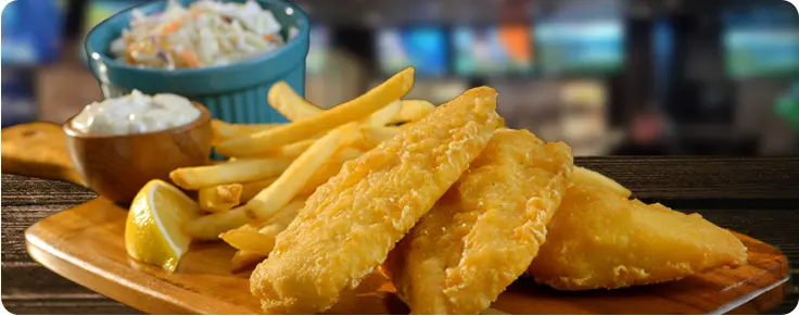 A plate of fried cod fillets with coleslaw and french fries
