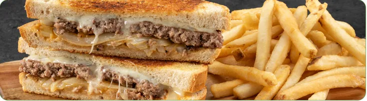 A stacked patty melt sandwich sits next to a mound of golden fries