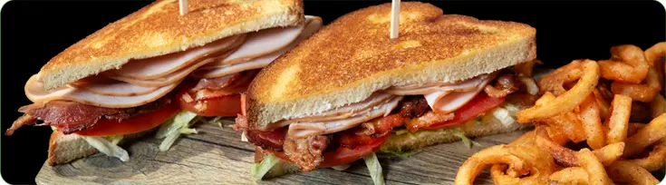 Two halves of a Turkey Club Sandwich next to fries