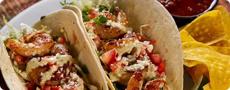 Two shrimp tacos on a plate with chips